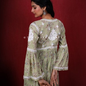 May include: A green floral print dress with white embroidery and a white lace trim. The dress has a V-neckline and bell sleeves. The dress is photographed from the back.