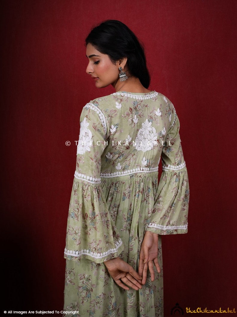 May include: A green floral print dress with white embroidery and a white lace trim. The dress has a V-neckline and bell sleeves. The dress is photographed from the back.
