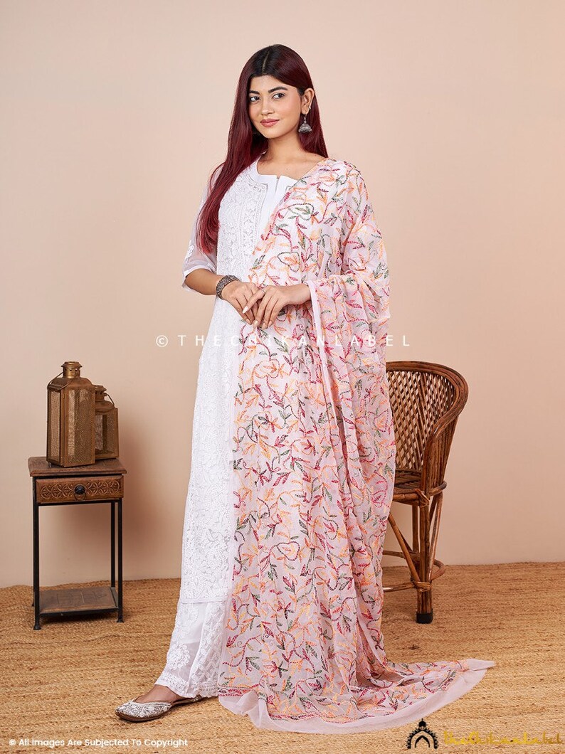 Pu&ograve; includere: Una kurta bianca ricamata con un dupatta ricamato con fiori rosa. La kurta ha una scollatura rotonda e maniche a tre quarti. Il dupatta &egrave; trasparente e presenta un delicato motivo floreale.