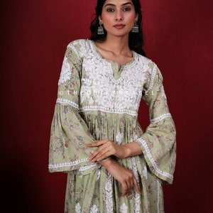 May include: A green floral print dress with white embroidery and bell sleeves. The dress has a V-neckline and a gathered waist. The model is wearing silver earrings. The text "@thechikanlabel" is visible on the dress.
