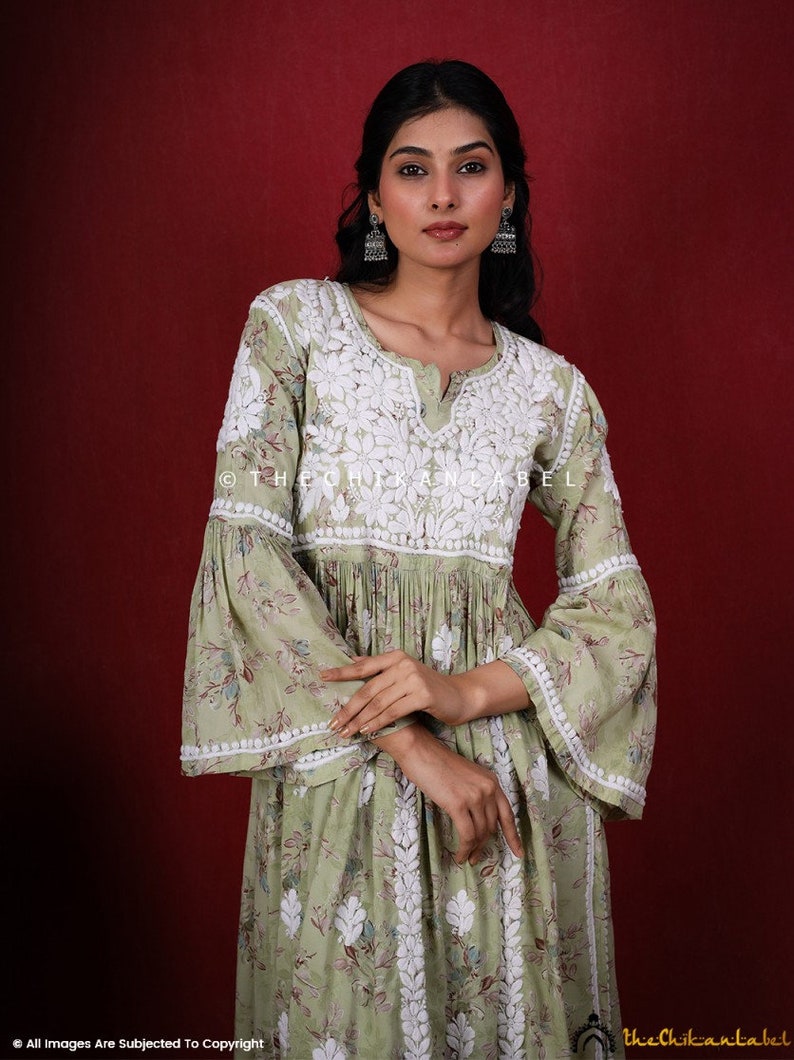 May include: A green floral print dress with white embroidery and bell sleeves. The dress has a V-neckline and a gathered waist. The model is wearing silver earrings. The text "@thechikanlabel" is visible on the dress.