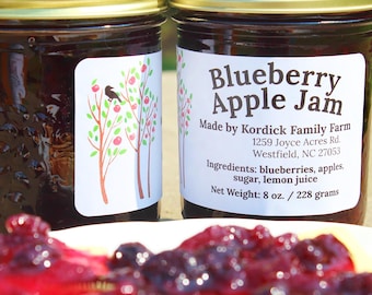 May include: Two glass jars of dark purple Blueberry Apple Jam with gold metal lids. The labels feature a tree illustration and text: Blueberry Apple Jam, Made by Kordick Family Farm, 1259 Joyce Acres Rd, Westfield, NC 27053, 8 oz. / 228 grams.