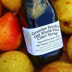 May include: A glass bottle of Grandpa Kordick's Old World Pear Cider Syrup with a green lid. The bottle is surrounded by pears. The label reads "Grandpa Kordick's Old World Pear Cider Syrup", "Ingredients: pear cider", "Net Volume: 12 oz./355 ml", "Made by Kordick Family Farm", "1259 Joyce Acres Rd. Westfield, NC 27053", "www.kordickfamilyfarm.com".