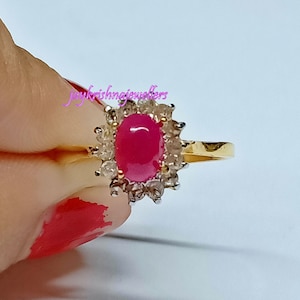 May include: A gold ring with a large oval pink ruby surrounded by smaller clear stones.