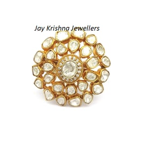 Puede incluir: Un anillo de oro con una gran piedra preciosa redonda blanca rodeada de piedras preciosas blancas m&aacute;s peque&ntilde;as. El anillo est&aacute; engastado con un dise&ntilde;o floral.