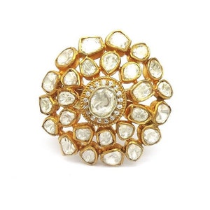 Puede incluir: Un anillo de oro con un gran diamante redondo y claro rodeado de diamantes m&aacute;s peque&ntilde;os en un patr&oacute;n floral.
