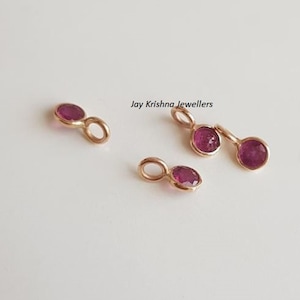 Op de afbeelding: Vier gouden hangers met een klein rood edelsteentje in het midden van elke hanger. Elke hanger heeft een lus om aan een ketting of armband te bevestigen.