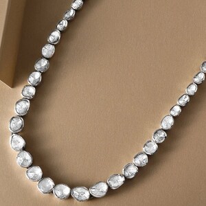 May include: A silver necklace with a row of white, rough-cut diamonds. The diamonds are set in a simple, elegant design.