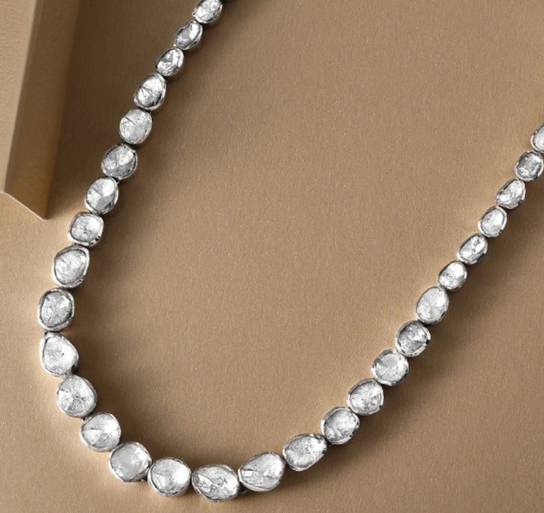 May include: A silver necklace with a row of white, rough-cut diamonds. The diamonds are set in a simple, elegant design.