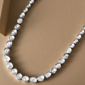 May include: A silver necklace with a row of large, clear, faceted diamonds. The diamonds are irregularly shaped and have a rough, natural look.