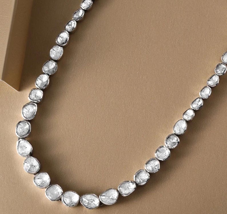 May include: A silver necklace with a row of large, clear, faceted diamonds. The diamonds are irregularly shaped and have a rough, natural look.