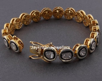 Puede incluir: Un brazalete de oro con cierre de broche y diamantes de forma ovalada engastados en un bisel de metal blanco. El brazalete tiene un diseño delicado e intrincado.