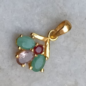 May include: A gold pendant with a cluster of green, pink, and red gemstones. The pendant is shaped like a V and has a loop at the top for attaching to a chain.