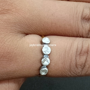Puede incluir: Un anillo de plata con cuatro piedras preciosas redondas y transparentes dispuestas en fila. El anillo está en un dedo, sobre un fondo neutro. El texto "jaykrishnajewellers" es visible.