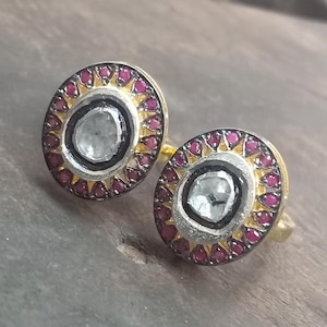 Peut inclure: Une paire de boucles d'oreilles en or de forme ronde. Chaque boucle d'oreille présente une grande pierre précieuse facetée transparente entourée d'un cercle de petites pierres précieuses rouges.