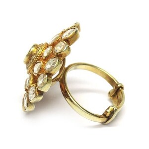 Puede incluir: Un anillo de oro con un gran engaste en forma de flor. El engaste est&aacute; adornado con numerosas piedras peque&ntilde;as y transparentes.