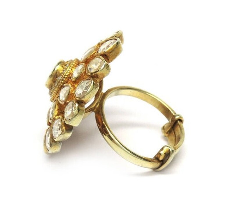 Puede incluir: Un anillo de oro con un gran engaste en forma de flor. El engaste est&aacute; adornado con numerosas piedras peque&ntilde;as y transparentes.