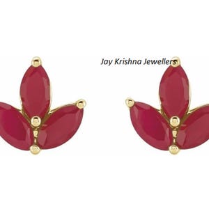 May include: A pair of gold-colored stud earrings, each featuring a three-petal design with vibrant red gemstones. The earrings have a floral shape, with small gold accents at the base of each petal. The text "Jay Krishna Jewellers" is visible.