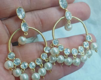 May include: Gold hoop earrings with white pearl drops and clear stones. The earrings have a dangling design with multiple layers of pearls and stones.