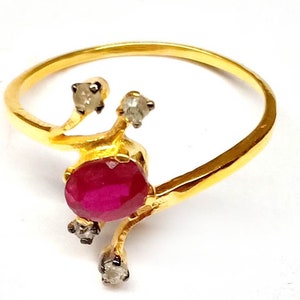 May include: A gold ring featuring a vibrant red ruby gemstone as the focal point. The ring has a unique design with three small, sparkling diamonds. The band is a simple, elegant gold.