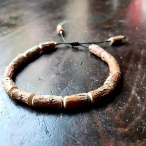 Könnte beinhalten: Ein braunes Holz-Armband mit einem schwarzen Kordelverschluss. Das Armband besteht aus kleinen, runden Holzstücken.