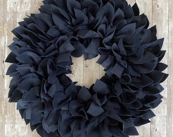 Może przedstawiać: Czarny wieniec z filcu o dużym, pełnym i puszystym wzorze. Wieniec wykonany jest z wielu pojedynczych liści z filcu, które są ułożone warstwami i nakładają się na siebie. Wieniec idealnie nadaje się do dodania odrobiny elegancji do każdego wystroju domu.