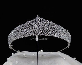 May include: A silver-toned tiara with a sparkling, crystal-like design. The tiara features a central, pointed design and is supported by a thin metal band. The text "MWBRIDALSTORE" is visible on the tiara. The tiara is displayed on a white surface with pearls.