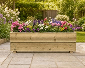 May include: A rectangular wooden planter box with horizontal grooved slats, filled with a vibrant assortment of blooming flowers in shades of pink, purple, white, and yellow, supported by small block feet on a stone patio surface.
