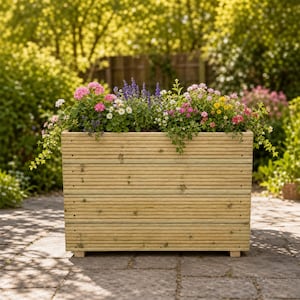 May include: A rectangular wooden planter box constructed from horizontal planks with visible grain and small feet. The planter is filled with a variety of colourful flowers including pink geraniums, purple salvia, white daisies, and small yellow blossoms.