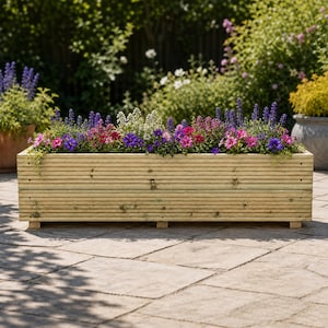 May include: A rectangular wooden planter box with horizontal ribbed slats, filled with a variety of colourful flowers including purple, pink, and white blossoms. The planter is constructed from light-coloured wood and rests on small block feet.