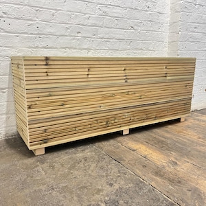 May include: A wooden storage bench with a slatted design. The bench has a natural wood finish and is sitting on a wooden floor.