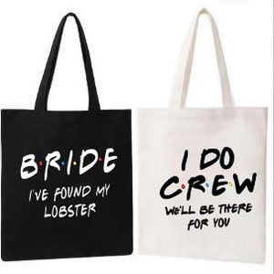 May include: Two tote bags, one black and one white, with text printed on them. The black bag says "Bride I've found my lobster" and the white bag says "I do Crew We'll be there for you".