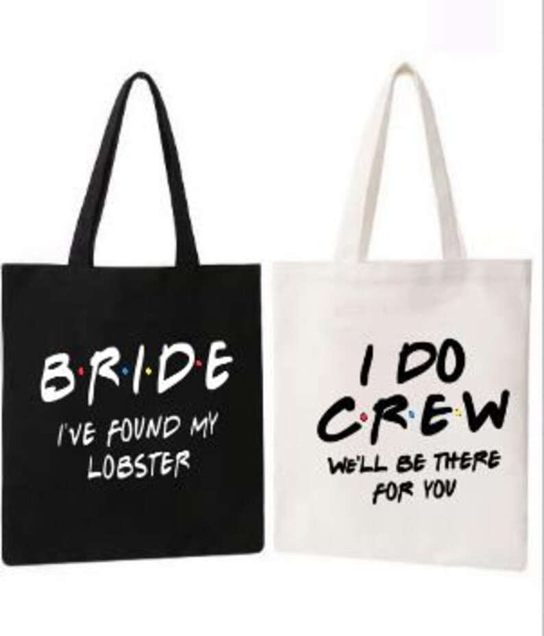 May include: Two tote bags, one black and one white, with text printed on them. The black bag says "Bride I've found my lobster" and the white bag says "I do Crew We'll be there for you".