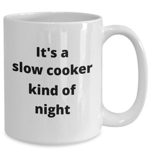 May include: White ceramic mug with a curved handle. The mug features the text "It's a slow cooker kind of night" in black, bold font. The mug is designed for hot beverages.