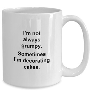 May include: White ceramic mug with a curved handle. The mug features black text that reads, "I'm not always grumpy. Sometimes I'm decorating cakes."
