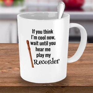 May include: White ceramic mug with a black text that reads "If you think I'm cool now, wait until you hear me play my Recorder." A brown recorder graphic is also on the mug. A silver spoon is inside the mug.