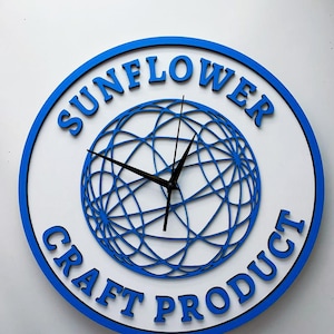 May include: A white clock with a blue rim and black hands. The clock face features a blue, circular design with a web-like pattern. The words "SUNFLOWER CRAFT PRODUCT" are written around the rim of the clock.