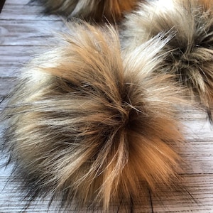 May include: A fluffy pom pom made of faux fur in shades of brown, black, and beige. The pom pom is soft and fluffy, and would be perfect for adding a touch of whimsy to a hat or scarf.