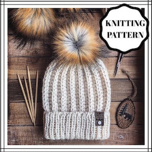 Puede incluir: Gorro de punto blanco con un pompón esponjoso marrón y blanco. El gorro tiene una textura acanalada y un pequeño parche de cuero marrón con el texto "NORTHSTAR" en él.