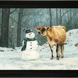 May include: A framed print showing a winter scene with a snowman and a cow. The snowman is wearing a black hat and scarf, and the cow has brown fur. Snow covers the ground, and trees are in the background. The artwork is signed.