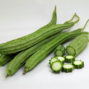 May include: A bunch of green loofah gourds, some whole and some sliced, on a white surface.