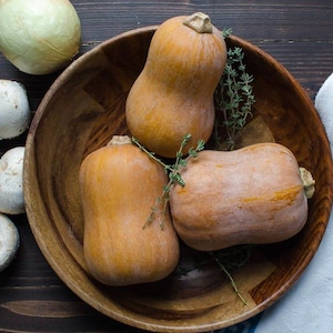 May include: Three whole butternut squashes in a wooden bowl with sprigs of fresh thyme.