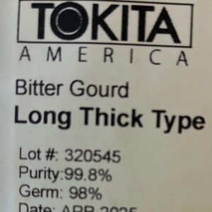 May include: A white label with black text. The text reads "TOKITA AMERICA", "Bitter Gourd Long Thick Type", Lot # 320545, Purity: 99.8%, Germ: 98%, and Date: APR 2025. The label is for a food product.
