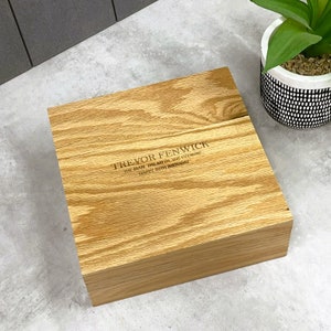 Könnte beinhalten: Eine hellbraune Holzbox mit eingraviertem Text auf dem Deckel: "TREVOR FENWICK THE MAN, THE MYTH, THE LEGEND HAPPY 80TH BIRTHDAY". Die Box steht auf einer grauen Oberfläche, im Hintergrund ein Blumentopf.