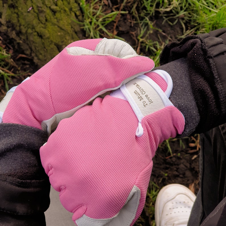 May include: A pair of pink fabric gloves with white accents. The gloves have a white label with the text "To Mum Love Out" on them.