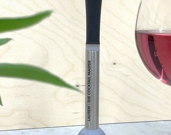 Puede incluir: Un machacador de cócteles plateado con una parte superior de goma negra y una inscripción personalizada que dice "Lauren - The Cocktail Master".