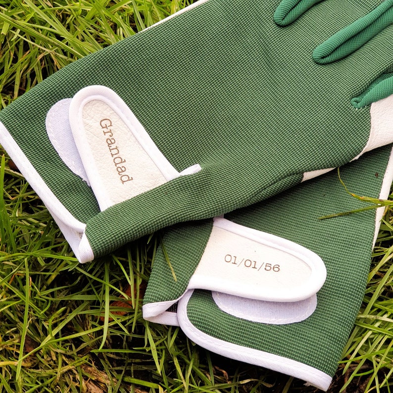 May include: A pair of green gardening gloves with white trim. The gloves have the words "Grandad" and "01/01/56" written on them.
