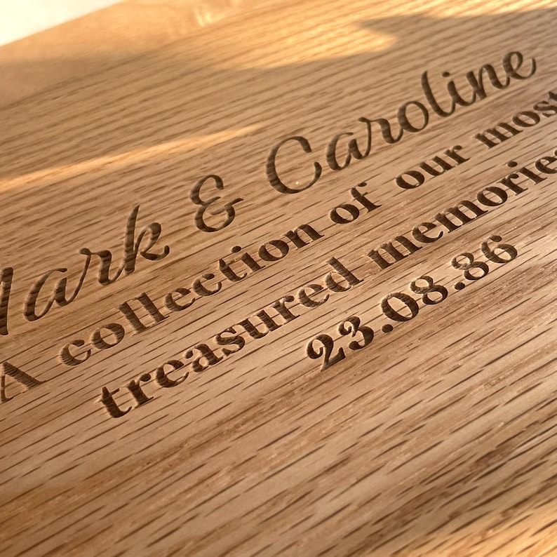 Pode incluir: Close-up de uma placa de madeira com texto gravado. O texto diz "Mark & Caroline, A collection of our most treasured memories, 23.08.86". A madeira tem um gr&atilde;o natural e uma cor castanha clara e quente.