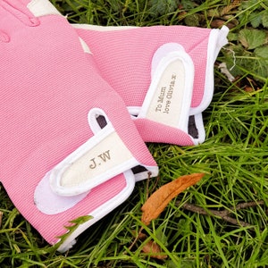 May include: A pair of pink gardening gloves with white trim. The gloves have the text "To Mum love Olivia x" and "J.W" written on them.