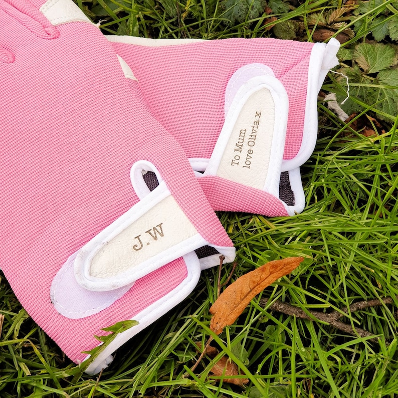 May include: A pair of pink gardening gloves with white trim. The gloves have the text "To Mum love Olivia x" and "J.W" written on them.